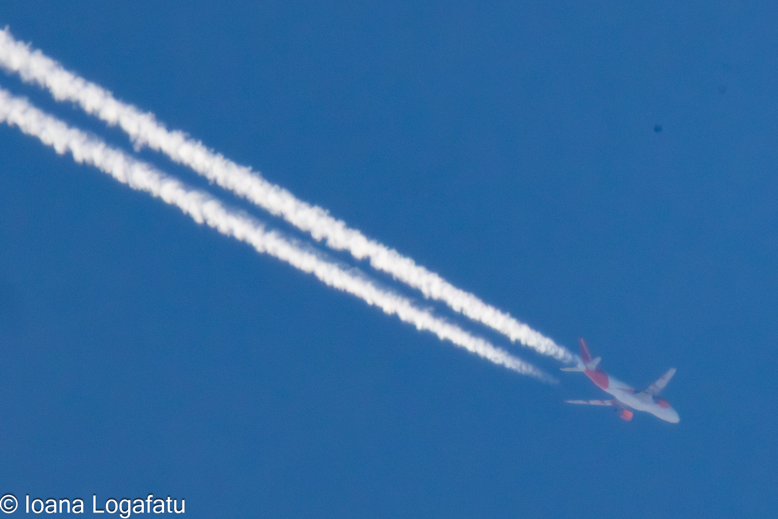 Airplane glides through clear blue sky with trails